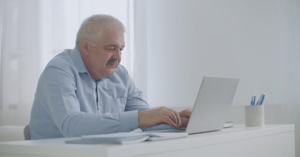 Orta yaşlı bir adam internet üzerinden e-posta teknolojisi kullanarak iletişim kuruyor, mesajlar yazıyor, evden çalışıyor. — Stok video