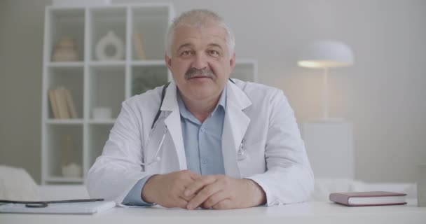 portrét mužského terapeuta mluví do kamery, sedí u stolu ve své kanceláři na klinice, dává doporučení