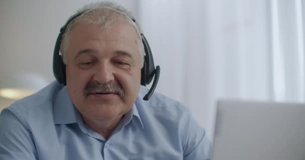 Homem gordinho de meia-idade com bigode está usando fones de ouvido com microfone para se comunicar com os colegas no chat online — Vídeo de Stock