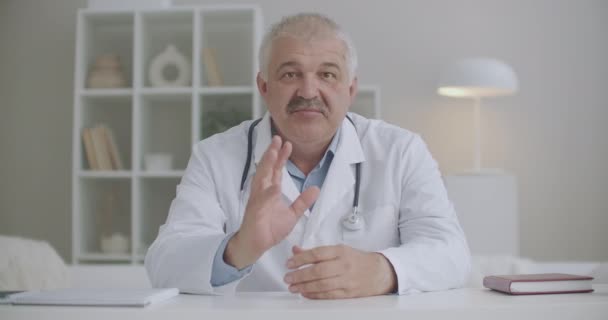 Männlicher Kinderarzt mittleren Alters berät sich online vom Büro in der Klinik aus, beantwortet Fragen und gibt Empfehlungen — Stockvideo