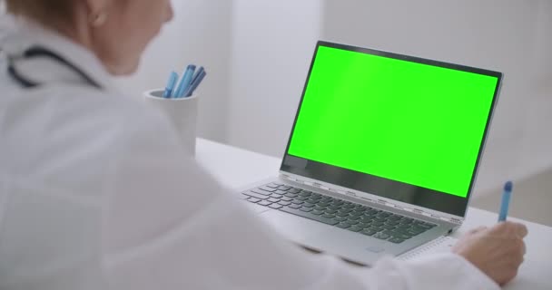 Γυναίκα ιολόγος παρακολουθεί σε απευθείας σύνδεση webinar, κοιτάζοντας πράσινη οθόνη του φορητού υπολογιστή για την τεχνολογία κλειδί chroma, γράφοντας σημειώσεις σε χαρτί και γνέφοντας — Αρχείο Βίντεο