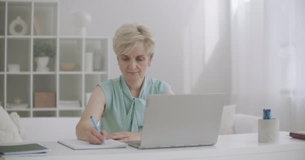 Mujer de mediana edad está trabajando con el ordenador portátil, ver webinar y escribir notas, autoeducación a distancia — Vídeo de stock