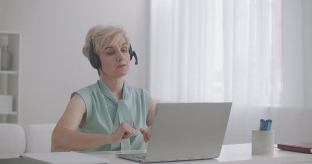 技術サポートやコールセンターの専門家はオンラインでクライアントに相談していますヘッドフォンを持つ女性はノートパソコンで電話に答えています — ストック動画