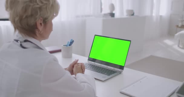 Medico donna sta ascoltando paziente durante la consultazione online, guardando lo schermo verde del computer portatile per la tecnologia chroma key, lavorando in remoto — Video Stock