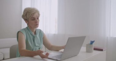 Yaşlanmış kadın öğretmen internette ders veriyor, dizüstü bilgisayarın web kamerasına, internetin uzaktan eğitimine, kadın portresine bakıyor
