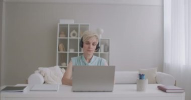 Psikolog internet üzerinden danışmanlık yapıyor. Kadın uzman bilgisayarın web kamerasına konuşuyor. Masada oturuyor.