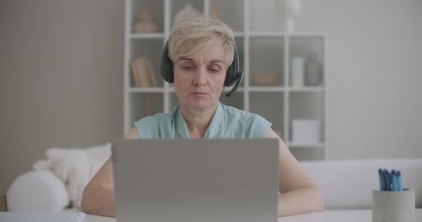 Femme âgée communique en ligne, en utilisant un ordinateur portable avec Internet et écouteurs avec microphone, chat en ligne, support technique — Video