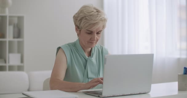 Contable anciana está trabajando con el ordenador portátil en la oficina, mujer está escribiendo en el teclado, utilizando Internet — Vídeo de stock