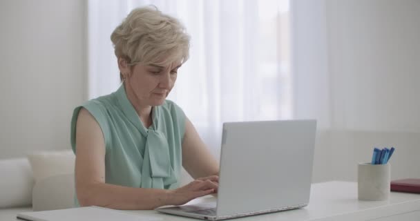 Anciana está trabajando de forma remota, utilizando el ordenador portátil con conexión a Internet para comunicarse, escribiendo mensaje en el chat en línea — Vídeo de stock
