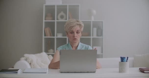 Anciana mujer está sentada en casa y charlando en línea por ordenador portátil con conexión a Internet, hablando con un amigo — Vídeos de Stock