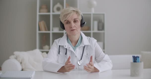 Mujer anciana profesora de medicina está llevando a cabo webinar o conferencia en línea, sentado en la oficina y mirando a la cámara — Vídeos de Stock