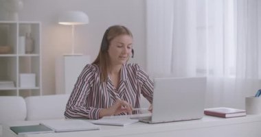 Genç bayan avukat internet üzerinden müşteriye danışmanlık yapıyor, kulaklıkla mikrofona konuşuyor ve notlar yazıyor.