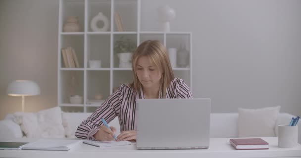 Educación a distancia de la mujer joven, que está aprendiendo por Internet, el uso de la computadora portátil y la escritura en el copybook, quedarse en casa — Vídeo de stock