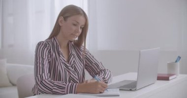 Genç kadın online ders notları alıyor, evde oturuyor ve bilgisayarını kullanarak uzaktan öğreniyor.