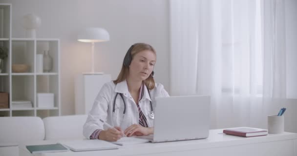 Kadın doktor hastalarla ya da iş arkadaşlarıyla bilgisayar üzerinden konuşuyor, uzaktan çalışıyor, teletıp hizmeti veriyor. — Stok video