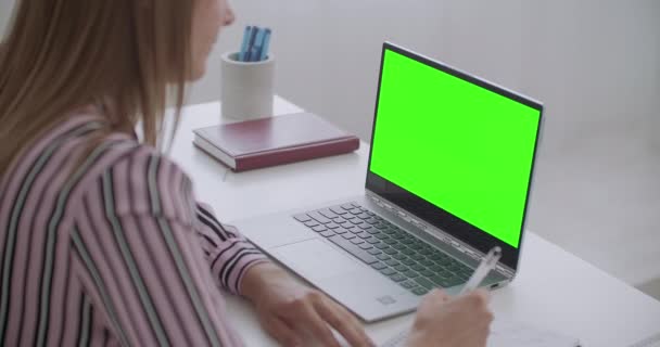 E-educação, mulher está vendo no laptop com tela verde para a tecnologia chave chroma, estudante do sexo feminino está escrevendo notas — Vídeo de Stock