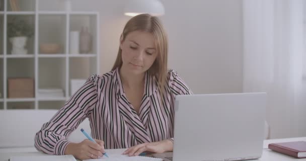 Samouk a e-learning, žena sleduje online školení na displeji notebooku a psaní na papíře — Stock video