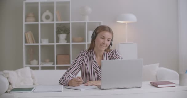 Especialista do sexo feminino de call-center ou suporte técnico está respondendo a chamada do cliente de casa, trabalhando remotamente, usando laptop — Vídeo de Stock