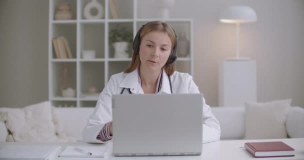 Consulta on-line com o médico, terapeuta do sexo feminino está pedindo paciente por videocall no laptop e escrever notas no copybook — Vídeo de Stock