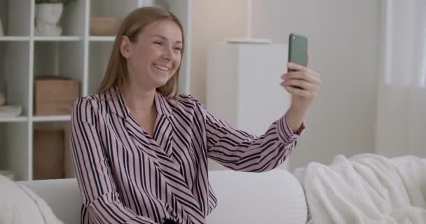 Jeune femme utilise l'appel vidéo dans le smartphone, assis à la maison et bavarder avec des amis par Internet pendant l'auto-isolement — Video