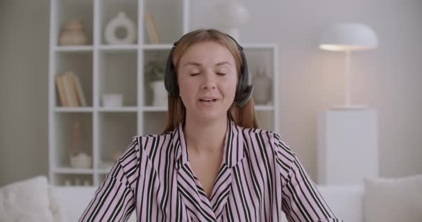 Νεαρή φιλική γυναίκα μιλάει κοιτάζοντας κάμερα, επικοινωνία σε απευθείας σύνδεση, χρησιμοποιώντας ακουστικά με μικρόφωνο — Αρχείο Βίντεο