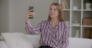 Genç bir kadın akıllı telefon kamerasıyla eğitim videosu çekiyor. Evde oturup selfie çekiyor.