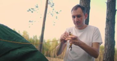 Ormanda yavaş çekimde çadır kuran bir adamın portresi.