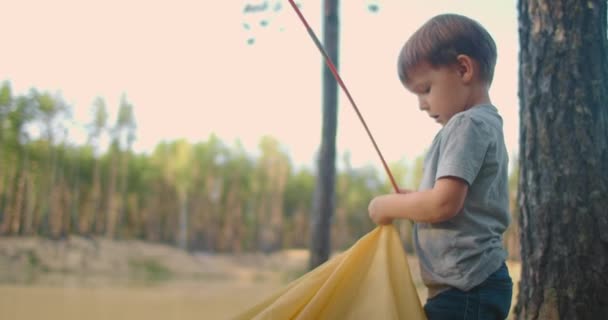 El niño ayuda a su padre a montar una tienda de campaña en el bosque. Enseñar a los niños y viajar juntos en un campamento de campaña — Vídeos de Stock