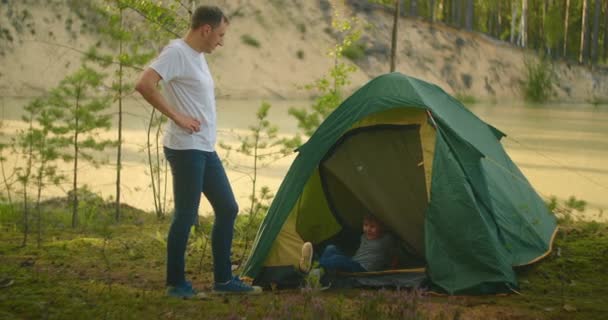 Boy climbs into a tent on the shore of the lake while traveling and relaxing with his father in nature — Stock Video