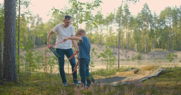 En far i slow motion och två barn satte upp ett tält i skogen under en helgresa. Faderskap och barn — Stockvideo