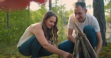 Bir çift adam ve bir kadın birlikte ormandaki çubuklardan ateş topluyor. Yürüyüşe çıkmış genç bir çift gece için ateş yakar ve doğada yemek pişirir.