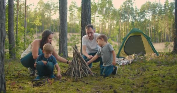 Family sits around a campfire on a summer evening. Children with their parents are resting in the woods. Weekend in nature in good company. Family frying sausages over a fire in the woods. — Stock Video