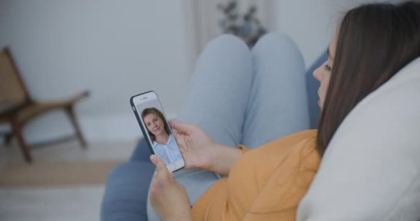 Bouclé jeune femme ayant chat vidéo avec des amis en utilisant une caméra de téléphone mobile tout en étant couché sur le lit. attrayant gai femme assise sur le canapé et avoir un appel vidéo avec des copines — Video