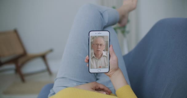 Vue sur l'épaule de la jeune fille vidéo appelant vieux père parent ou ami mature en utilisant l'application de chat de conférence en ligne sur l'écran de téléphone mobile au bureau à la maison. Concept de vidéocall familial — Video