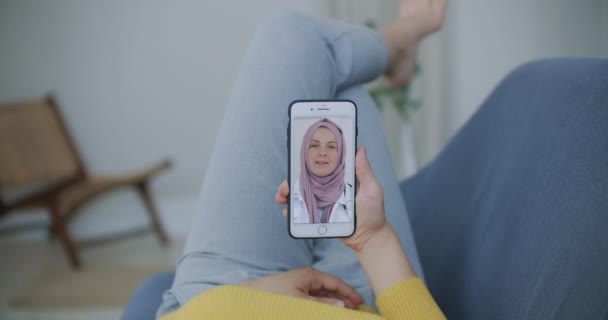 Una ragazza parla con un dottore in hijab usando un link video. Lavoro a distanza di un medico donna musulmana — Video Stock