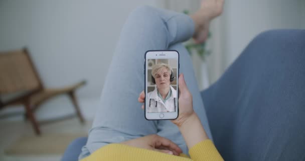 Arzt oder Therapeut helfen, Stress durch Coronavirus-Krise zu überwinden Videokonferenzschaltung online Live-Talk mit Frau sitzen auf Sofa Couch zu Hause mit Smartphone Arztkonsultation. — Stockvideo