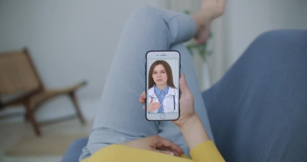 Arzt oder Therapeut helfen, Stress durch Coronavirus-Krise zu überwinden Videokonferenzschaltung online Live-Talk mit Frau sitzen auf Sofa Couch zu Hause mit Smartphone Arztkonsultation. — Stockvideo