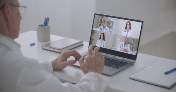 Elderly doctor talking head shot portrait four diverse medical workers in white coats take part in distant talk, engaged in group video call. Videoconferencing, concilium remote communication concept — Stock Video