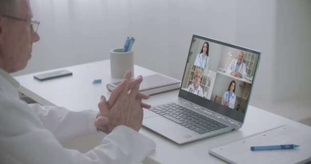 Vue par-dessus l'épaule du client assis au bureau recevoir des consultations médicales en ligne de divers spécialistes. Homme écouter les médecins sur les mesures de précaution du virus corona, visioconférence ordinateur portable webcam vue — Video