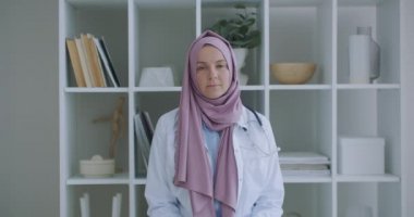 Kameraya bakarken tesettürlü kadın doktor kameraya bakar ve hastayı dinler. Video konferans dinleyicisi. Başörtüsü içinde bir doktorun portresi