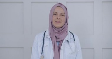 Video konferans yoluyla tesettürlü Arap Müslüman kadın. Müslüman kadın bir doktorun portresi. Kadın sağlık uzmanı ameliyat önlüğü ve hastane merdivenlerinde oturan bir tesettür giyiyor.
