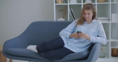 Çekici kızıl saçlı genç kız evde koltukta oturmuş telefonla gülümsüyor. Mutlu hissediyorum. İletişim kadını cep telefonu ya da akıllı telefondan mesaj arıyor..