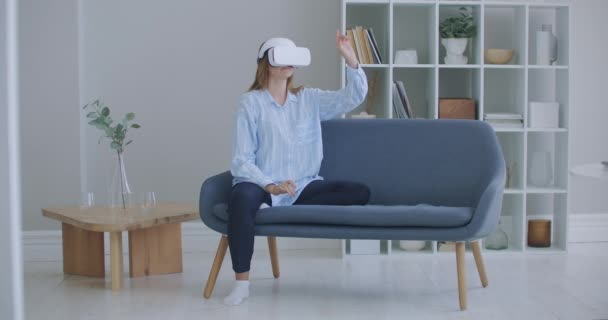 Mulher usando óculos simulador de realidade virtual jogar jogos de vídeo na sala de estar, feminino se sentir feliz usando relaxar o tempo deitado no sofá em casa. Estilo de vida mulheres relaxar em casa conceito. — Vídeo de Stock