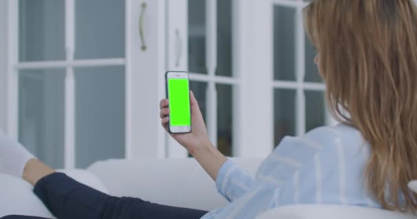 Femme utilisant téléphone portable écran vert vertical. Femme tenant dans la main gadget portable fermer à l'intérieur salon à la maison. Maquette pour suivre ou regarder du contenu. Chambre floue sur le fond — Video