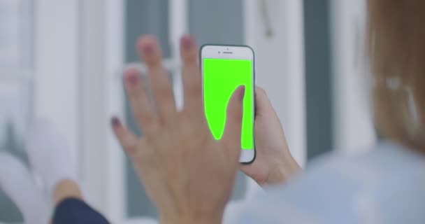 妇女使用视频呼叫移动电话垂直绿色屏幕.女性手持便携式小玩艺儿靠近室内客厅。用于跟踪或观看内容的模拟. — 图库视频影像