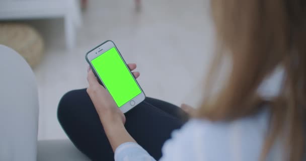 Kvinne som bruker og ser smart ut på den grønne skjermen hjemme. Ung jente holder tilbake smarttelefonen med grønt skjerm om kvelden. – stockvideo