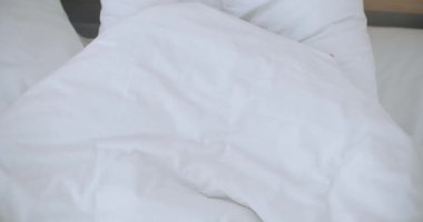 Bronz tenli, yatakta battaniyenin altında yatan ve altından bakan kadın. Güzel genç bir kadın battaniyenin altından dışarı bakıyor, kameraya gülümsüyor..