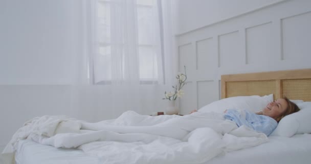 Una joven se despierta por la mañana en el hotel y se regocija sorbiendo y sonriendo — Vídeo de stock