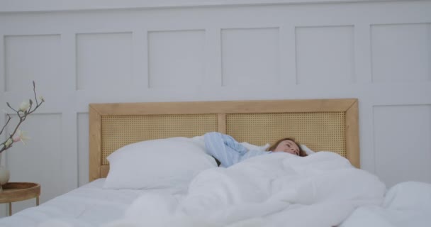 Una giovane donna si sveglia a letto la mattina sorridendo e facendo stretching. Buongiorno e buon giorno. Buon giorno. — Video Stock