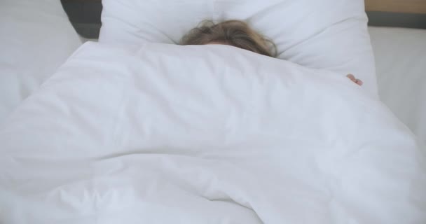 Glad kvinna som kikar ut ur sin filt i sängen och ler. Kikade under täcke och log — Stockvideo